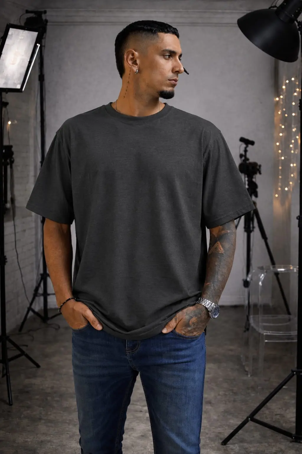 Hombre de perfil luciendo camiseta oversize gris oscuro de algodón con cuello redondo, corte relajado y jeans azules en estudio.