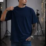 Hombre usando camiseta oversize azul oscuro de algodón en estudio fotográfico con luces y trípodes.