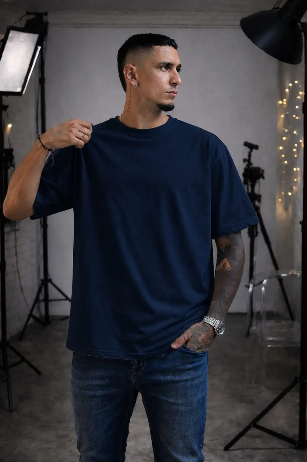 Hombre usando camiseta oversize azul oscuro de algodón en estudio fotográfico con luces y trípodes.