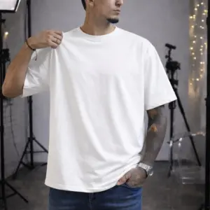 Hombre de piel morena con tatuajes viste camiseta oversize blanca de algodón con cuello redondo, en estudio de fotografía.