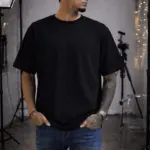 Hombre modelando camiseta oversize negra de algodón en estudio con luces.