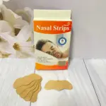 Caja naranja con seis tiras nasales de color beige y diseño ergonómico sobre superficie blanca, acompañadas de varios parches apilados.