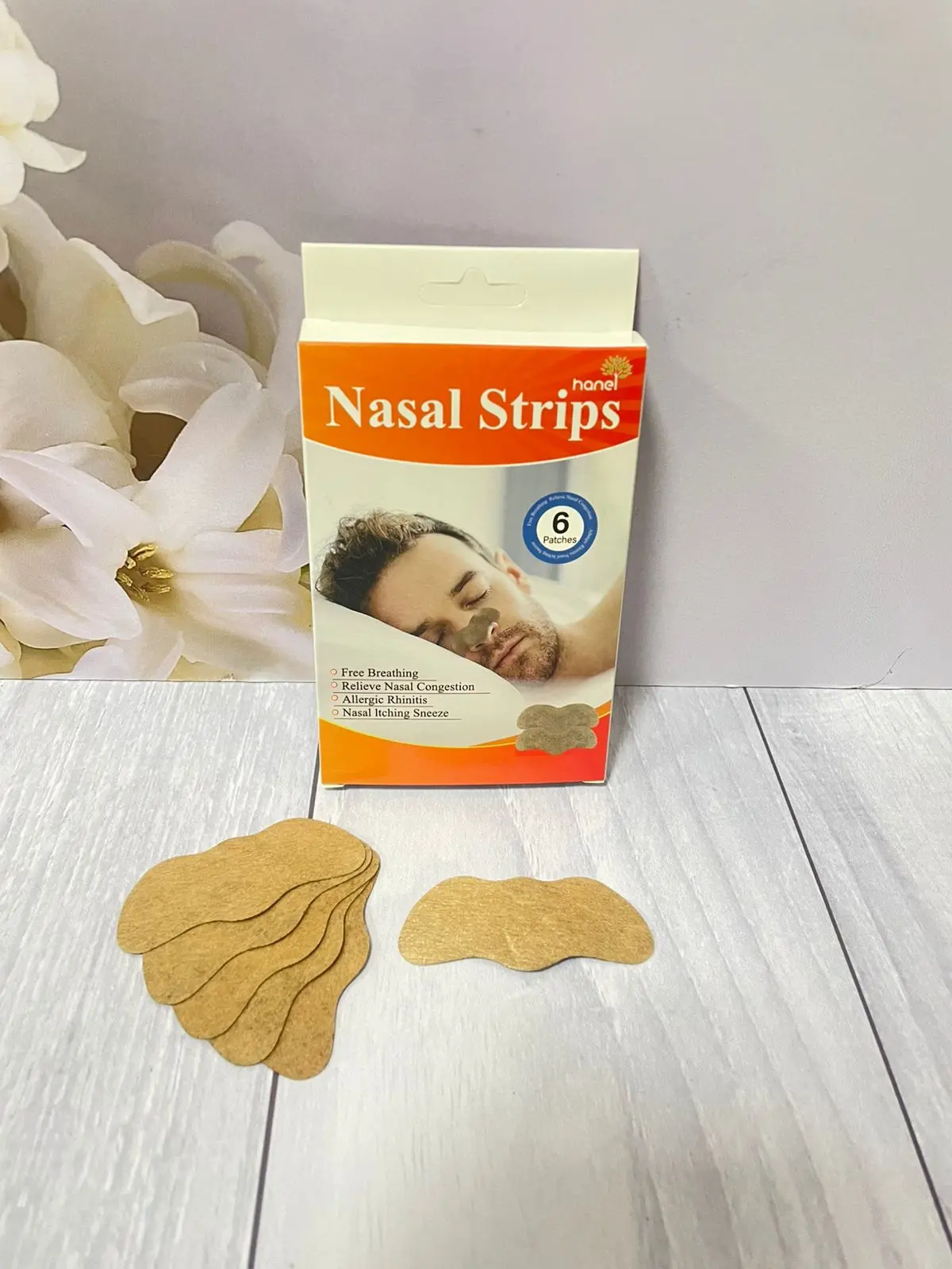 Caja naranja con seis tiras nasales de color beige y diseño ergonómico sobre superficie blanca, acompañadas de varios parches apilados.