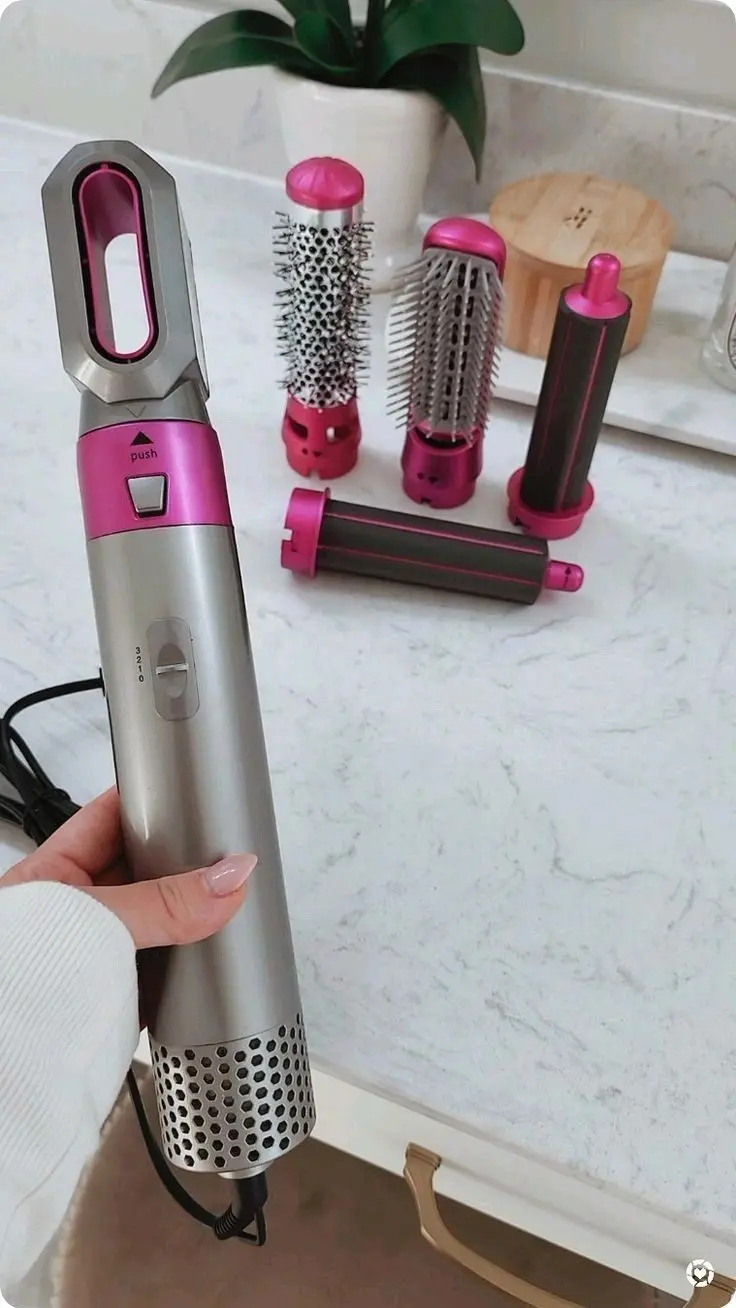Cepillo moldeador eléctrico gris y fucsia con cuatro accesorios para peinar sobre superficie de mármol.