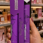 Set de crema corporal y perfume de 35 ml en empaque morado con silueta femenina, sostenido por una mano frente a estantes de fragancias.