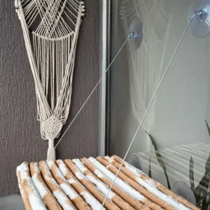 Hamaca para gato beige con textura acanalada, suspendida de un ventanal mediante ventosas y cuerdas finas para aprovechar el espacio vertical.