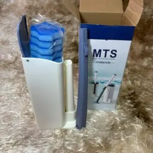 Escobilla para baño con soporte blanco, mango azul, repuestos de esponja azul en bolsa y caja MTS sobre alfombra beige de textura suave.