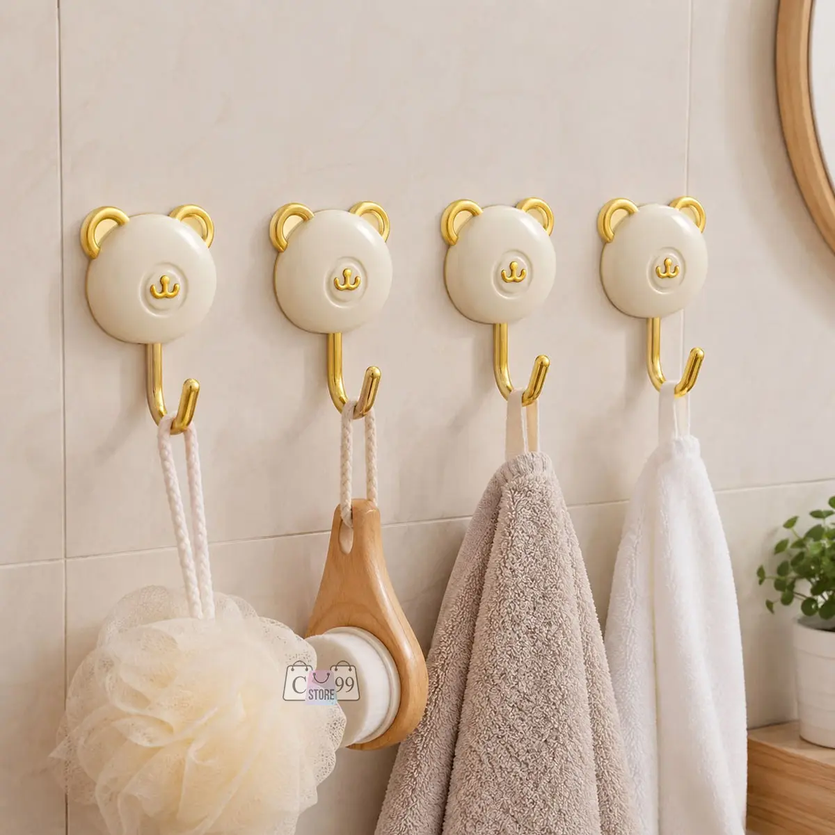 Ganchos adhesivos decorativos con forma de oso crema y detalles dorados en pared de baño, sosteniendo esponja, cepillo y toallas.