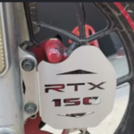 Protector metálico plateado para mordaza frontal AKT RTX 150 con grabado láser, montado sobre el freno de disco.