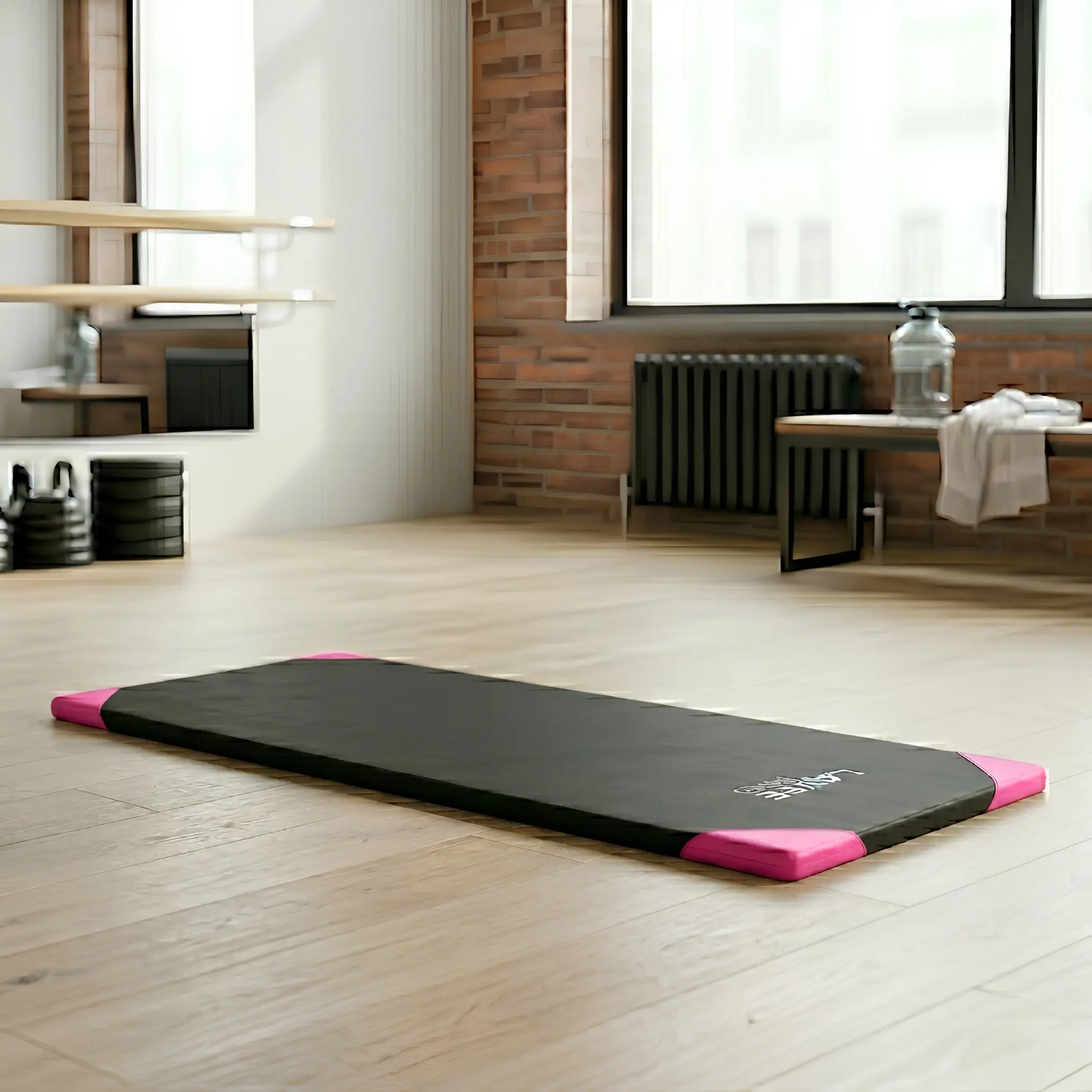 Colchoneta deportiva negra con refuerzos fucsia en esquinas y logotipo blanco, sobre piso de madera en estudio.