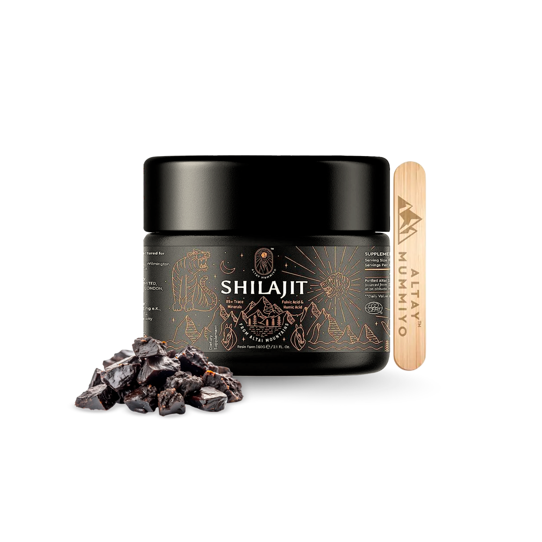 Frasco negro de Shilajit con ilustraciones doradas, espátula de madera y trozos de resina mineral oscura en primer plano sobre fondo blanco.