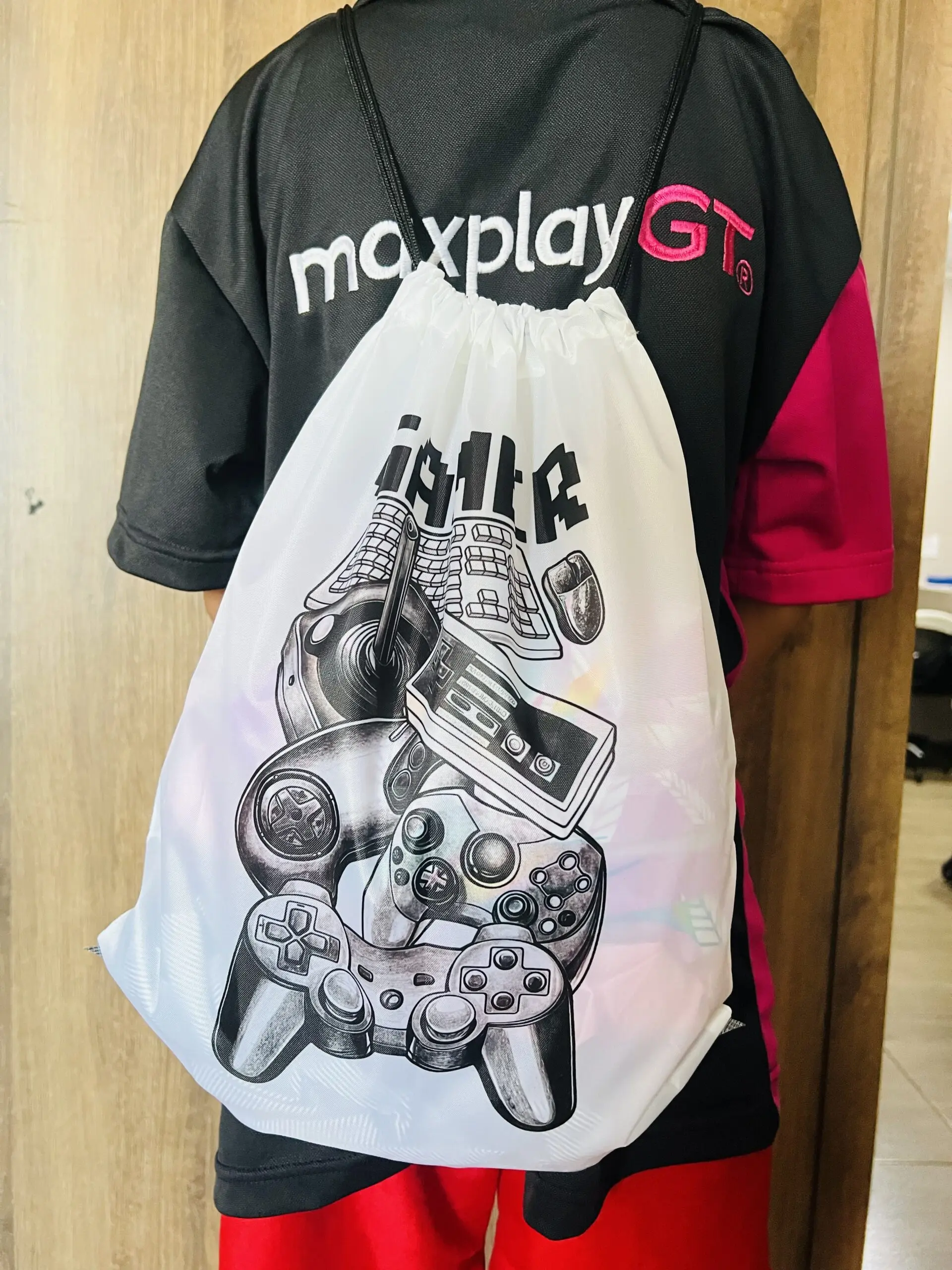 Mochila tipo saco para gamer semi impermeable blanca con estampado negro de controles y accesorios de videojuegos, portada en la espalda.