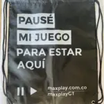 Mochila tipo saco negra semi impermeable con cordones y texto en blanco PAUSÉ MI JUEGO PARA ESTAR AQUÍ y logo maxplay.