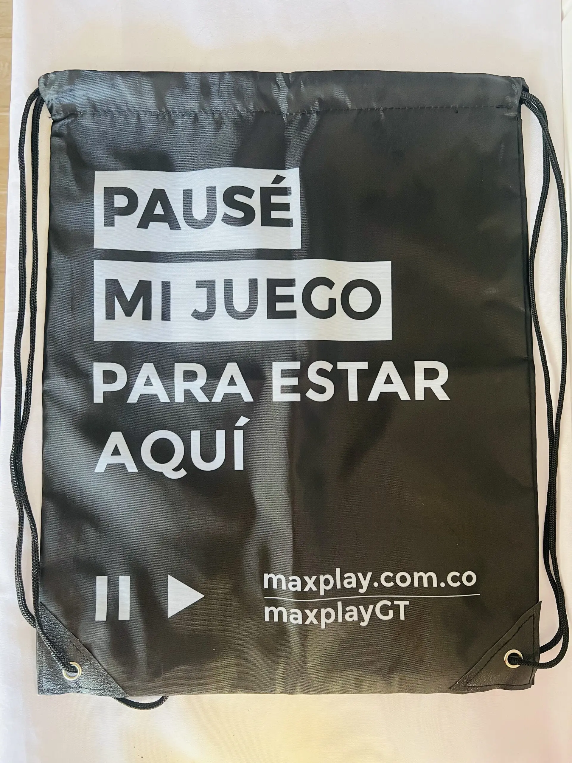 Mochila tipo saco negra semi impermeable con cordones y texto en blanco PAUSÉ MI JUEGO PARA ESTAR AQUÍ y logo maxplay.