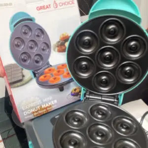 Máquina eléctrica para mini donas color turquesa con placas negras antiadherentes de siete moldes abiertas, junto a su caja de empaque.