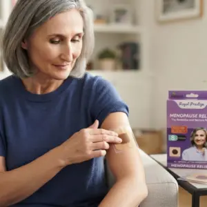 Mujer madura aplicando parche transdérmico natural morado para menopausia en su brazo con caja de 8 unidades sobre mesa blanca.