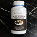 Frasco blanco de Evoralay con 60 cápsulas de aceite de semilla negra etíope, etiqueta negra con de semillas sobre mármol negro.