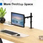 Soporte de escritorio negro para monitor de 15 a 30 pulgadas con brazo ajustable y base de sujeción, instalado en una mesa de madera clara.