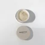 Polvo suelto traslúcido Montoc con tapa beige y envase transparente que muestra el tamiz, ideal para sellar el maquillaje con acabado mate natural.