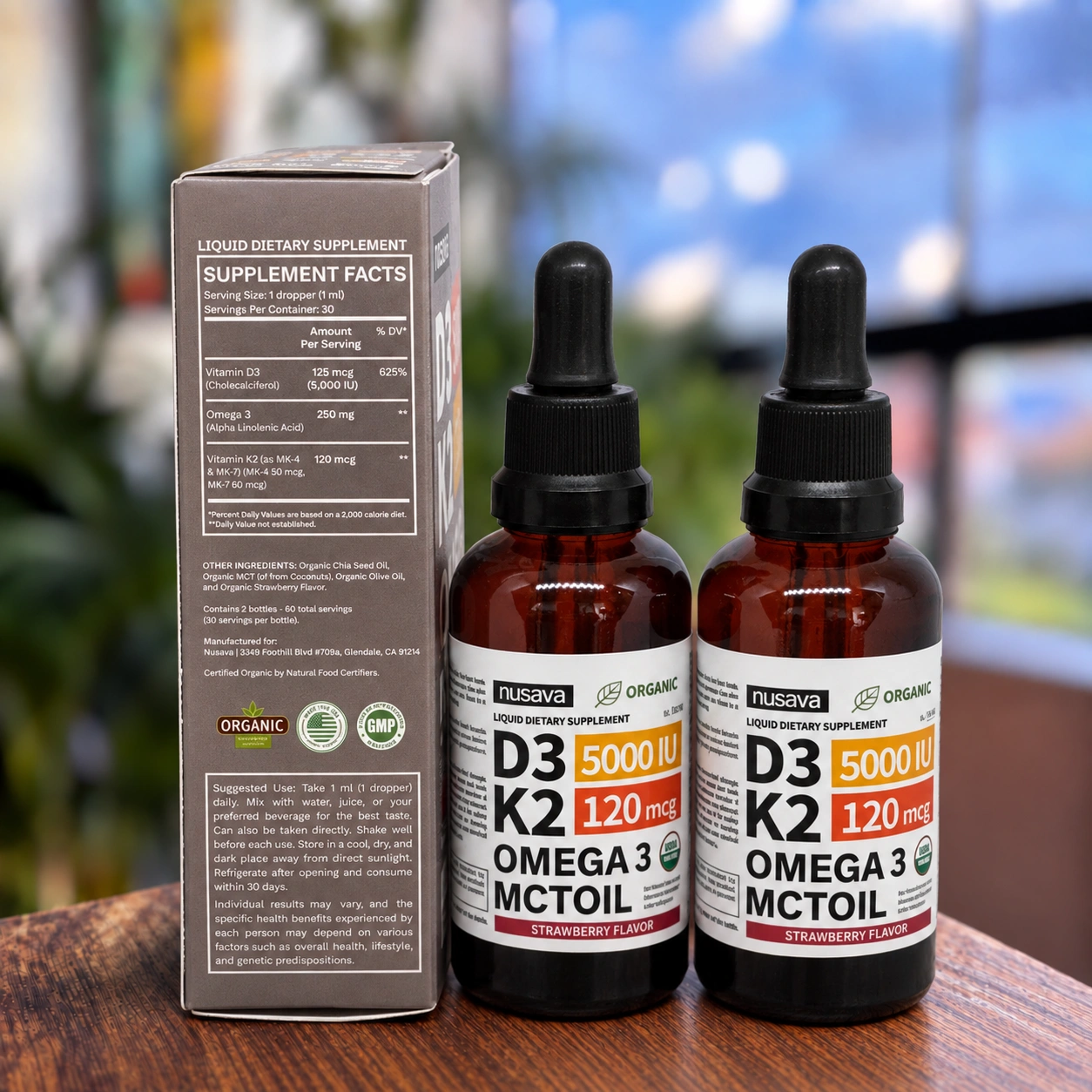 Set de dos frascos de suplemento líquido Nusava D3 K2 Omega 3 con aceite MCT, sabor fresa, junto a su caja con tabla nutricional sobre mesa de madera.