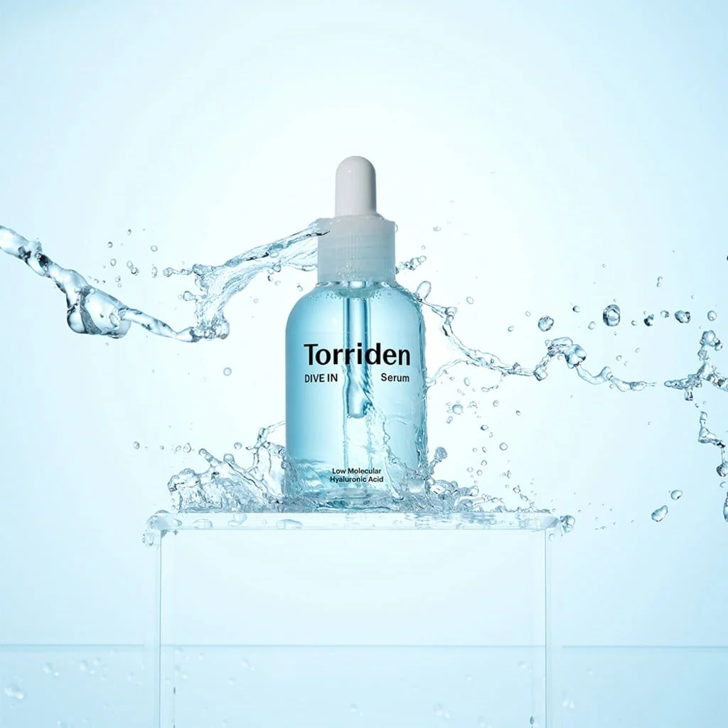 Sérum hidratante Torriden DIVE IN en frasco azul con gotero, rodeado de salpicaduras de agua sobre un pedestal transparente.
