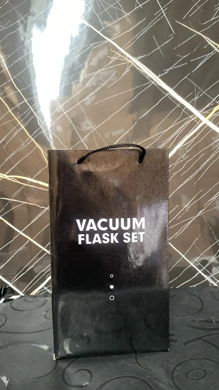 Bolsa de regalo de cartón negro brillante con el texto en blanco Vacuum Flask Set, asas negras y fondo texturizado.