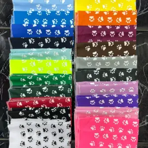 Pañoletas para perros apiladas en múltiples colores brillantes con estampado de huellas blancas y costuras en los bordes.
