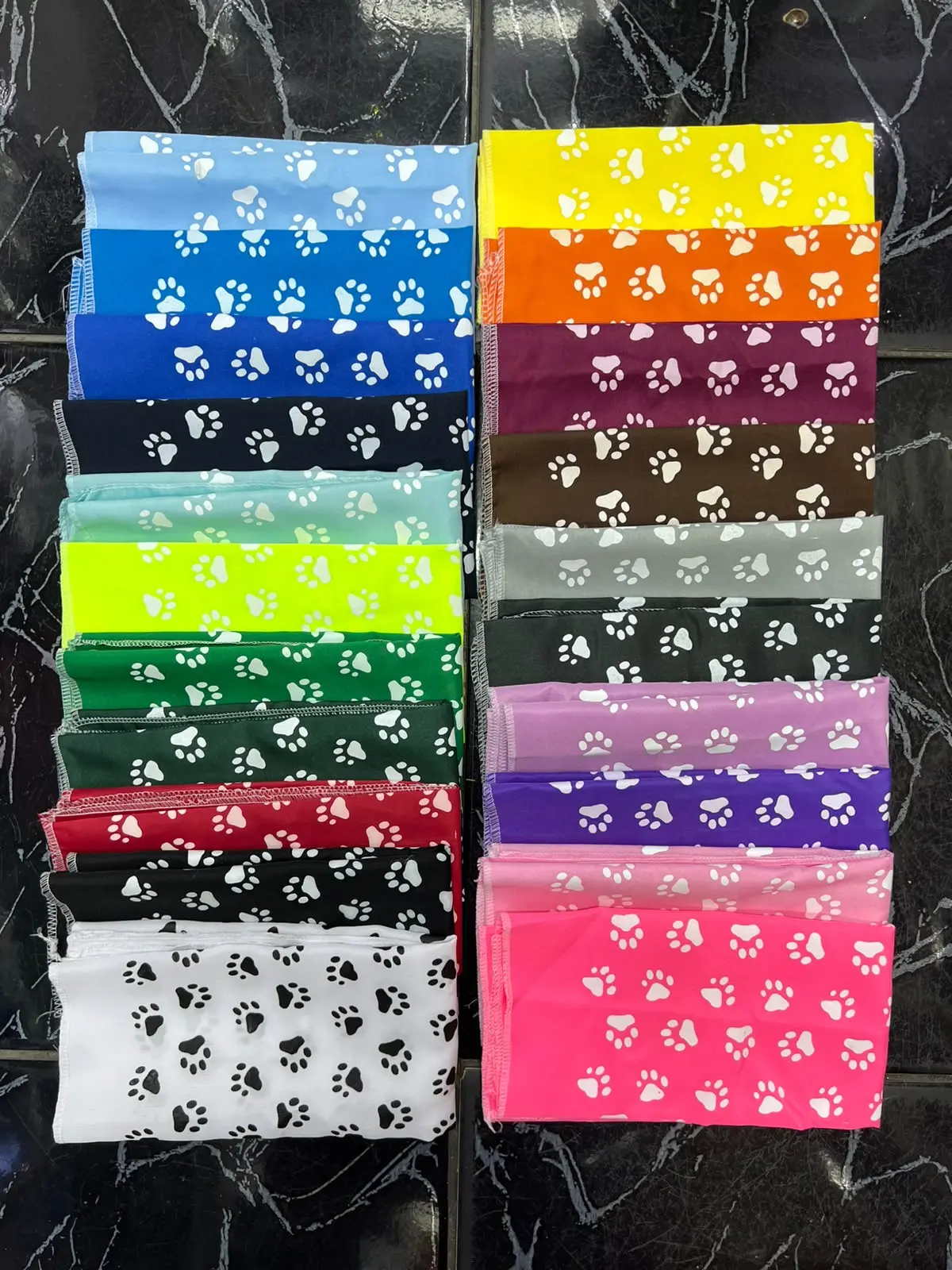 Pañoletas para perros apiladas en múltiples colores brillantes con estampado de huellas blancas y costuras en los bordes.