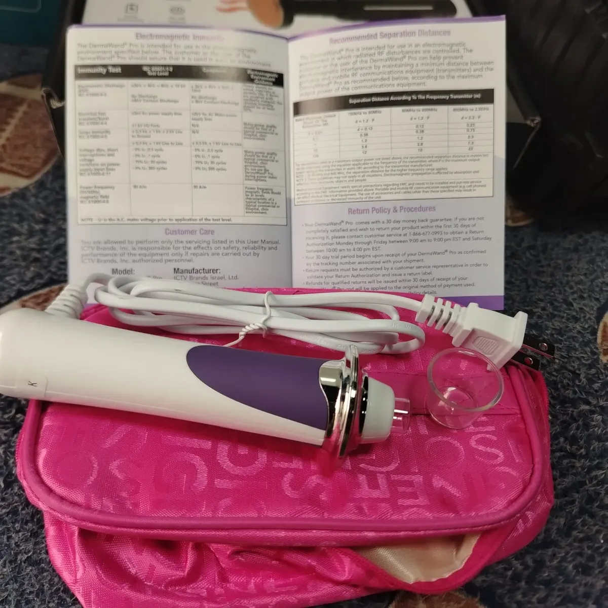 Dispositivo portátil de radiofrecuencia facial Derma W Pro en color blanco y morado con cable de corriente, accesorio de vidrio, estuche rosa y manual abierto.