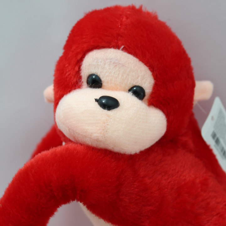 Peluche de mono rojo con rostro y orejas color durazno, textura de felpa suave y ojos negros, en primer plano.