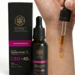 Frasco de aceite de Sacha Inchi con CBD 40% de 25 ml junto a su caja, con un gotero aplicando una gota del producto sobre la piel para uso tópico.