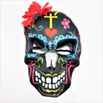 Máscara de calavera negra estilo Catrina con decoraciones coloridas, cruz amarilla, corazón rojo y una flor roja grande en el lateral superior.