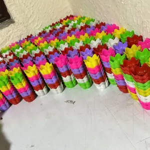 Set de portavelas plásticos en forma de flor, apilados en múltiples colores vibrantes sobre una mesa blanca, ideales para evitar derrames de cera.