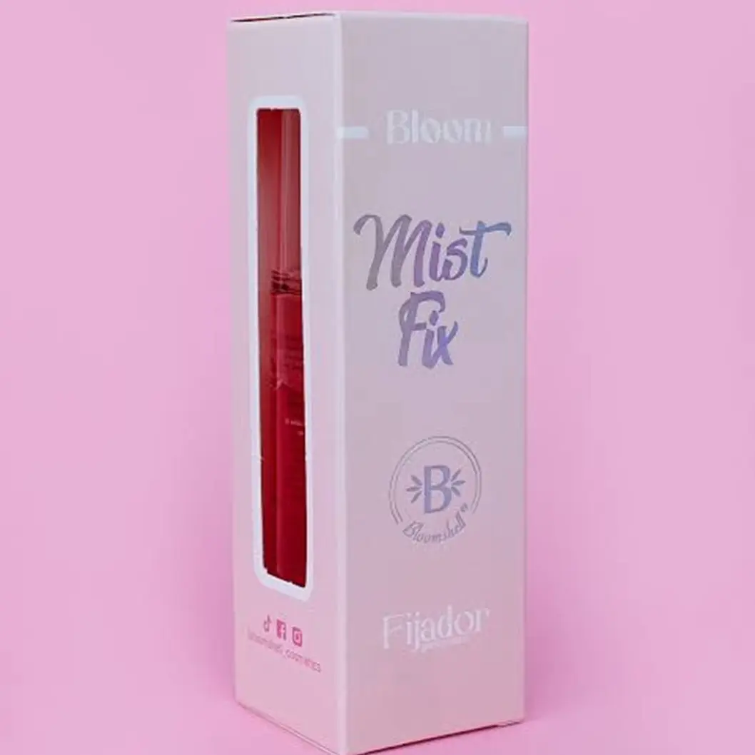 Caja rosa de Bloomshell Mist Fix con ventana lateral que muestra el envase rojo del fijador hidratante facial.
