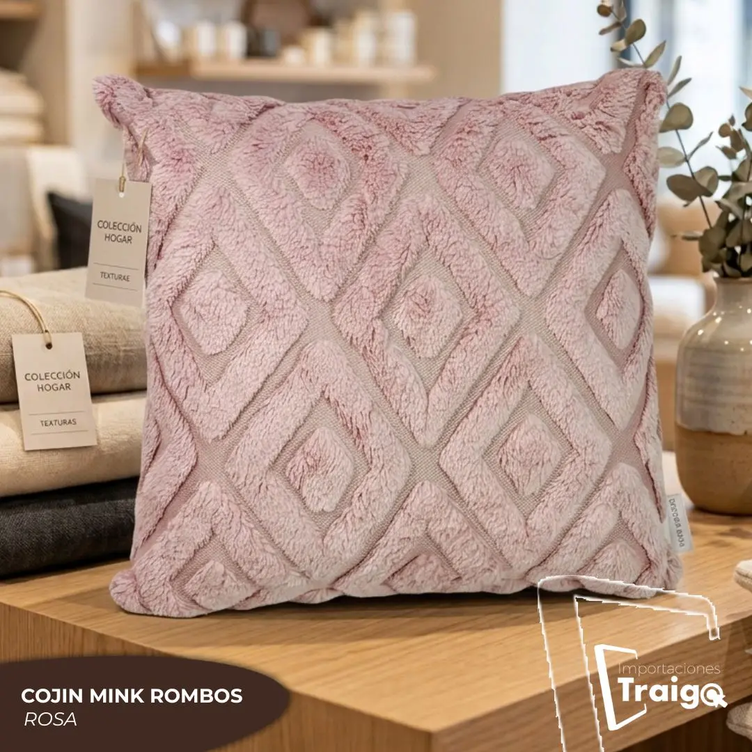 Cojín decorativo rosa de 45x45 cm en tela mink con relieve de rombos, exhibido sobre una mesa de madera junto a etiquetas de colección y un jarrón.