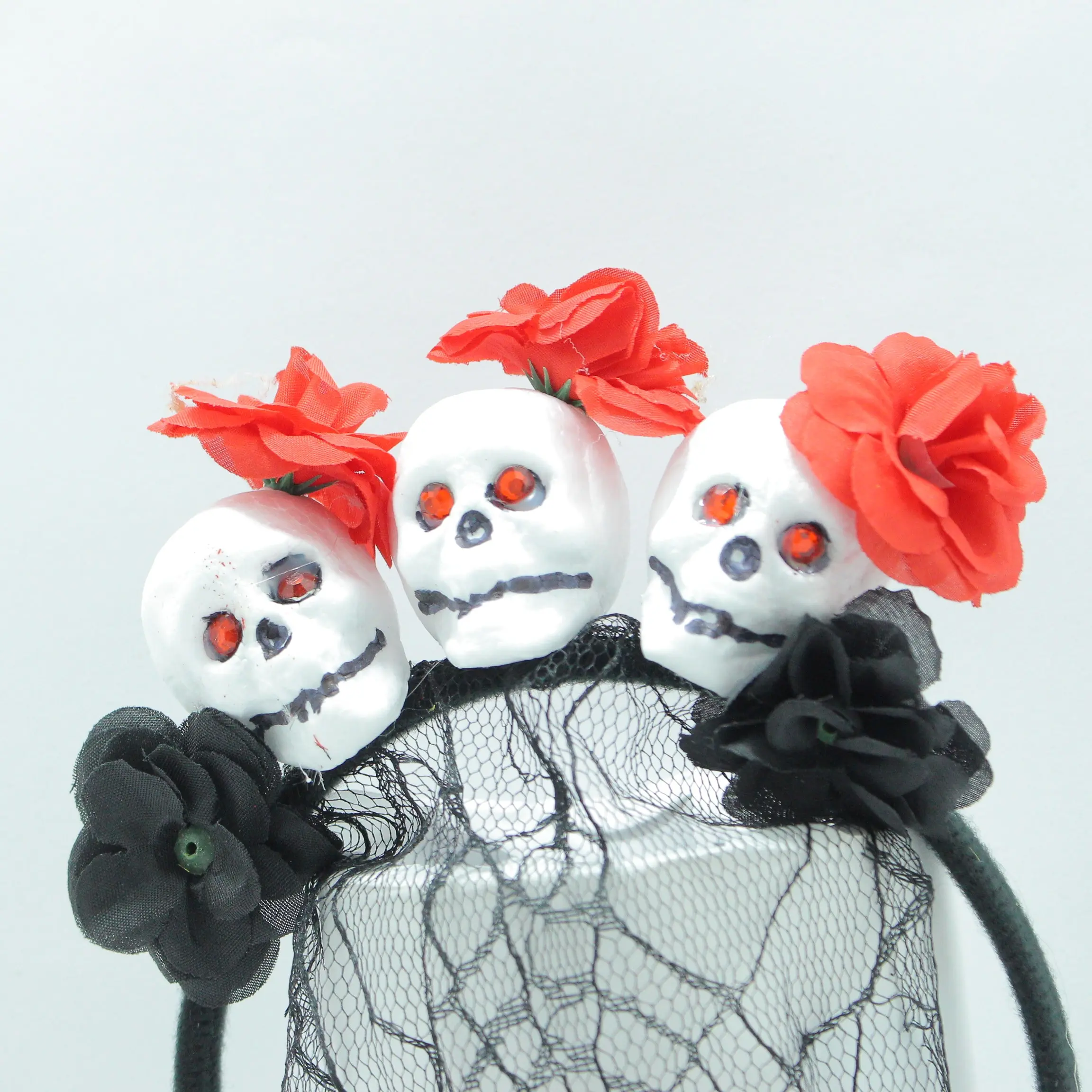 Diadema gótica con tres calaveras blancas de ojos rojos, decoradas con rosas rojas y negras, y velo de malla negra.