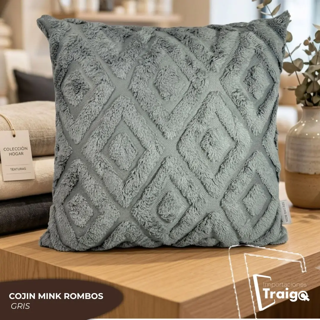 Cojín decorativo gris de 45x45 cm con textura suave tipo mink y diseño de rombos en relieve, exhibido sobre una mesa de madera junto a otros textiles.