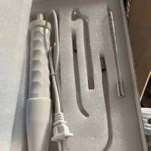 Varita facial de alta frecuencia blanca con cable y tres electrodos de vidrio de distintas formas dispuestos en su caja organizadora de espuma protectora.