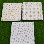 Tres cojines navideños de pelo sintético blanco con estampados dorados de hojas y copos de nieve sobre césped verde.