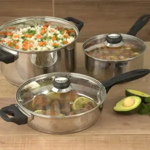 Batería de cocina de acero inoxidable con olla, sartén y cacerola tapadas, llenas de comida sobre una mesa de madera.