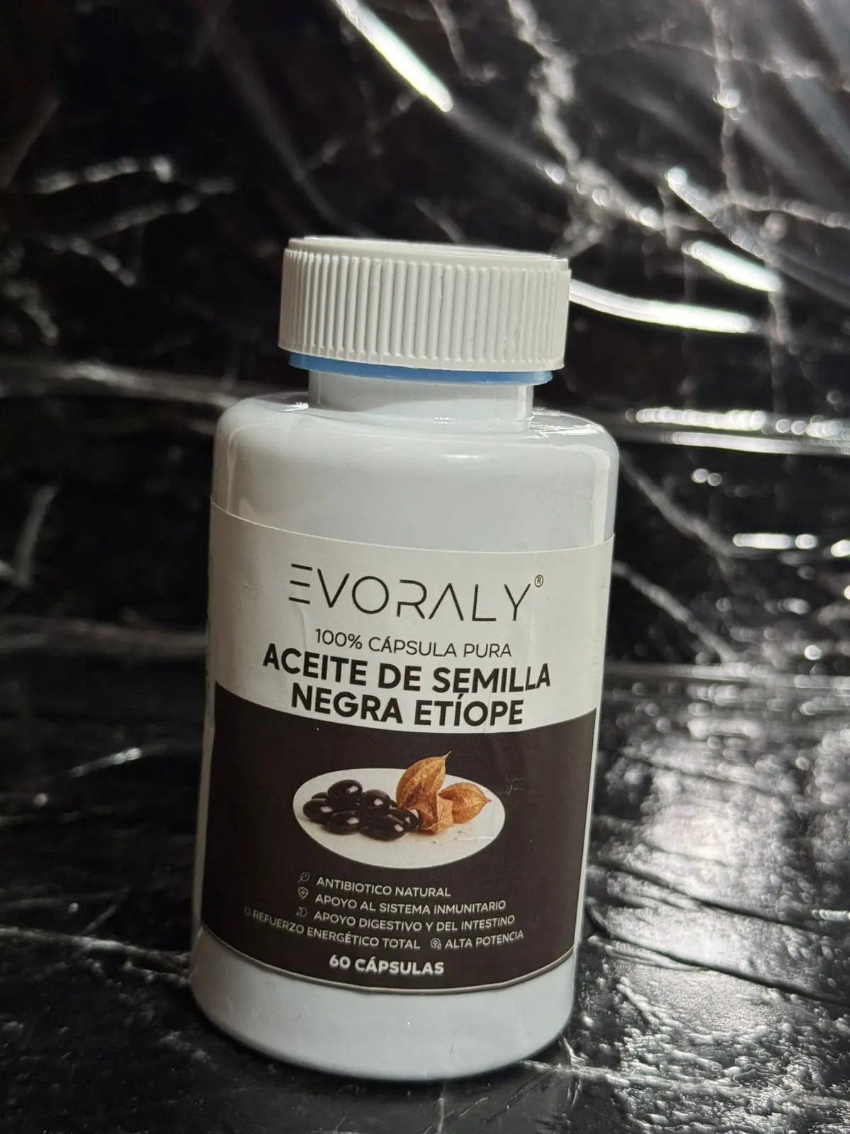 Frasco blanco de suplemento Evoraly con etiqueta café, conteniendo 60 cápsulas de aceite de semilla negra etíope, sobre superficie oscura.