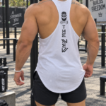 Camiseta esqueleto blanca deportiva con diseño negro en la espalda, vista posterior resaltando la musculatura en un parque de calistenia.