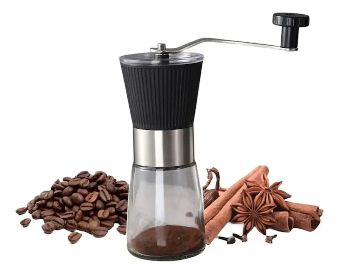 Molino de café manual negro con cuerpo de vidrio y manivela metálica, acompañado de granos de café y especias sobre fondo blanco.