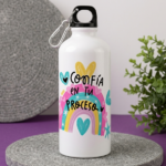 Termo metálico blanco con diseño de arcoíris acuarela y frase "Confía en tu proceso", tapa negra con mosquetón, sobre base de piedra gris.