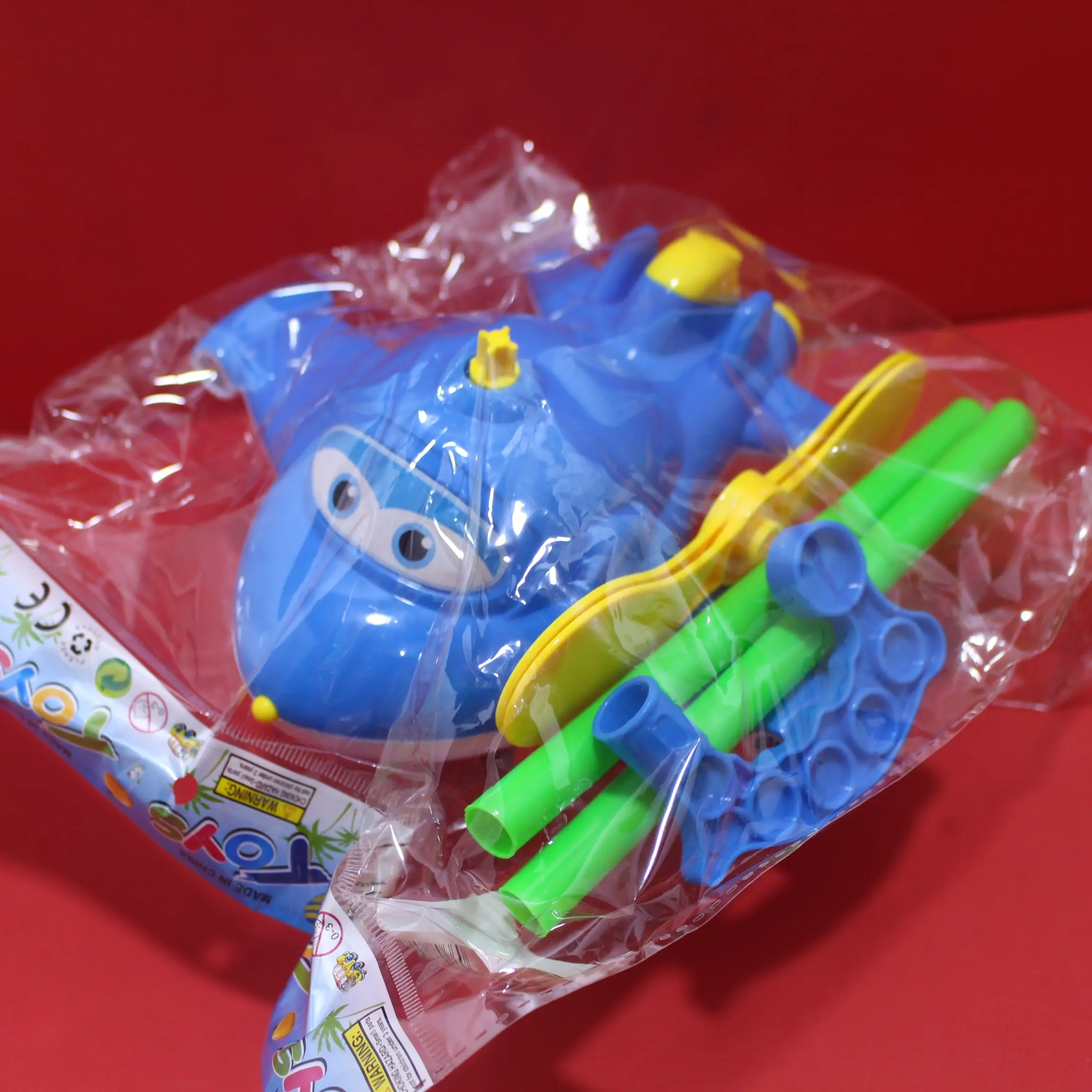 Set de andador en forma de avión azul con hélice amarilla, tubos verdes y piezas plásticas, empacado en bolsa transparente.