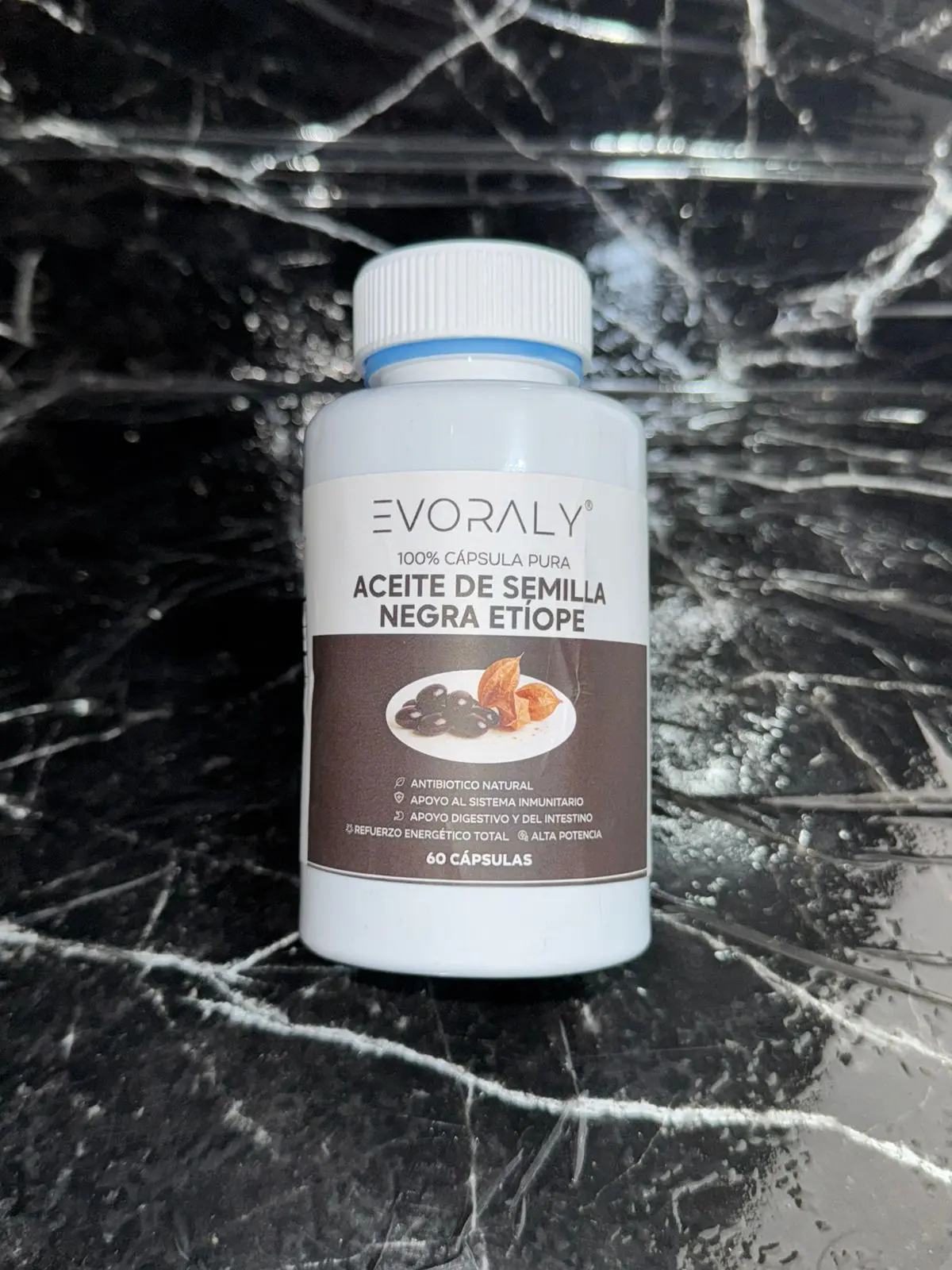 Frasco blanco de suplemento de aceite de semilla negra etíope Evoralý con 60 cápsulas, sobre fondo de mármol negro con vetas blancas.