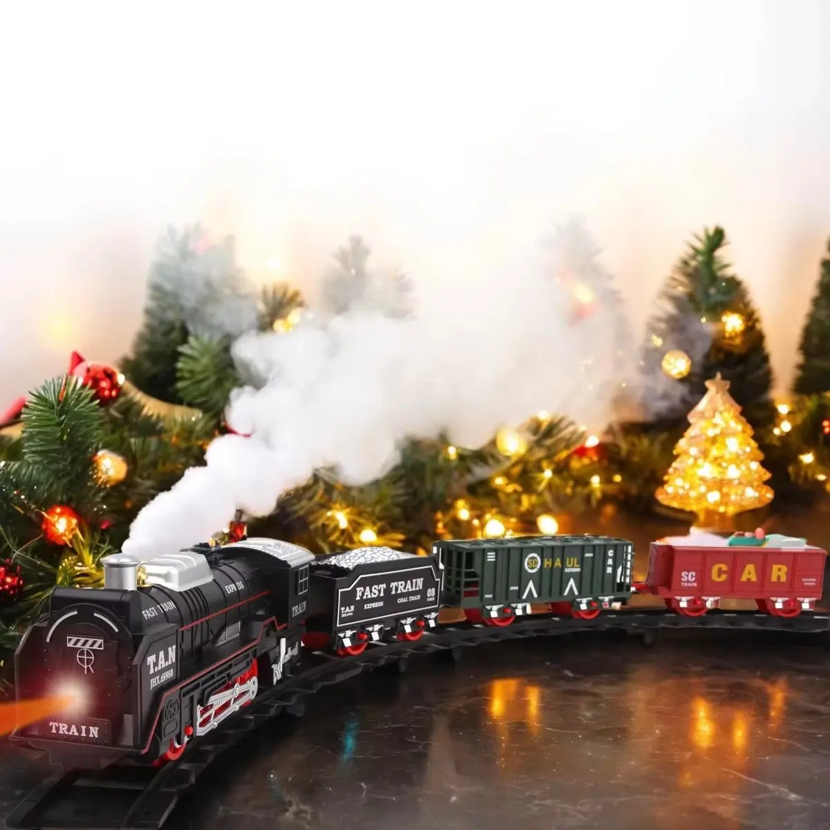 Tren eléctrico infantil con locomotora negra, vagones verde y rojo, efecto de humo blanco y luces cálidas en un decorado navideño.