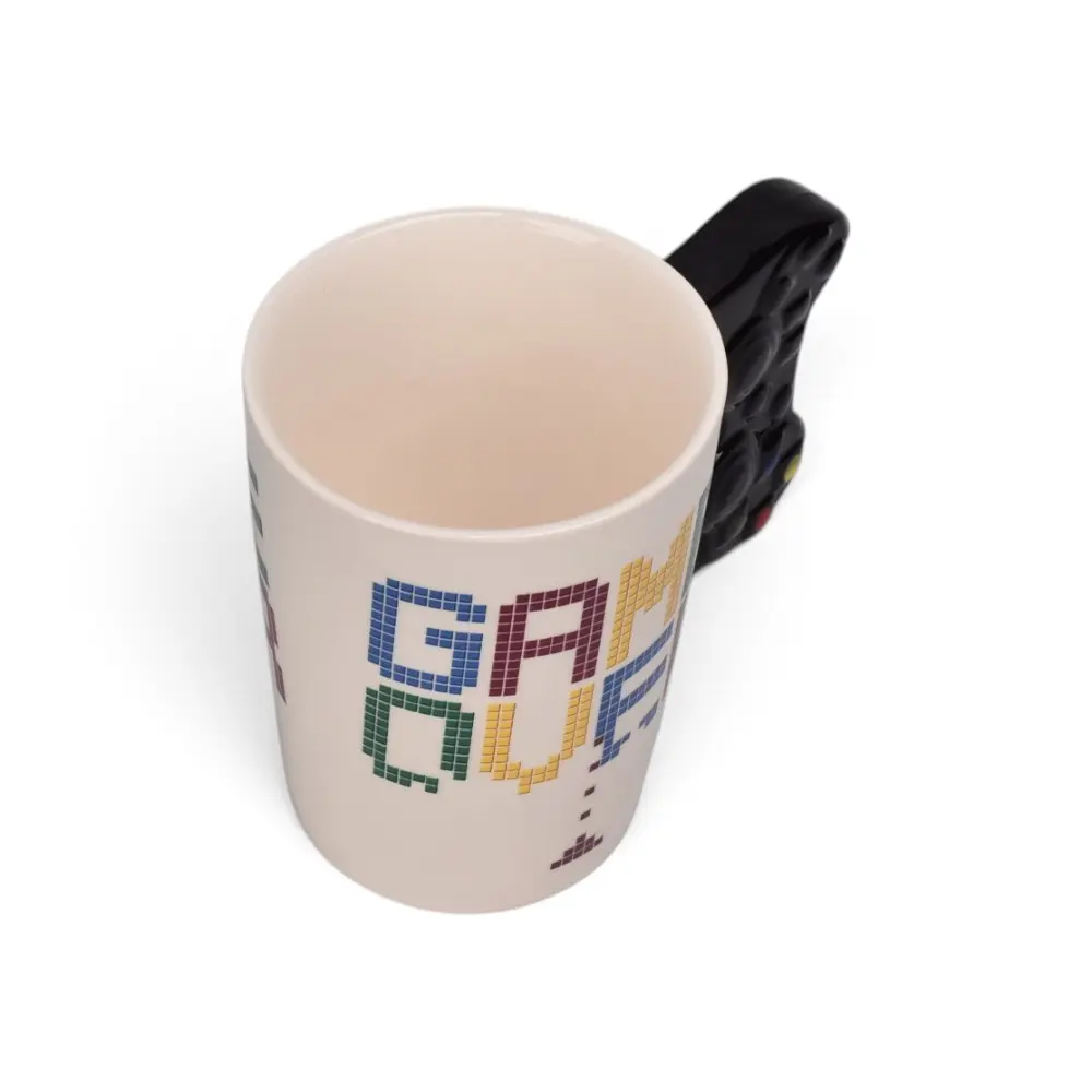 Taza de cerámica blanca con diseño píxel art de color azul, rojo y amarillo con la palabra gamer over, y asa negra en forma de control de videojuegos.