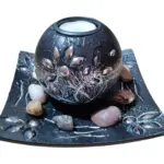 Centro de mesa decorativo de resina negra con detalles plateados, portavelas esférico y base con piedras naturales de colores.