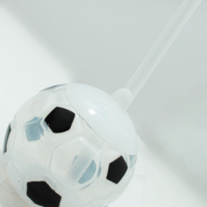 Termo infantil esférico transparente con diseño de balón de fútbol blanco y negro, tapa superior blanca y pitillo plástico incorporado.